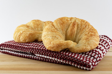 Two croissant rolls on a red and white towel on wooden surface.  White background.