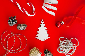 Wooden decoration in the form of a Christmas tree on a red background surrounded by Christmas elements. Place for text.