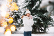 © anatoliycherkas - Outdoor close up portrait of young beautiful happy smiling girl wearing white knitted beanie hat, scarf and gloves. Model posing in park with Christmas lights. Winter holidays concept.