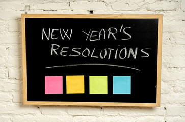 New Year resolutions written with chalk on blackboard with blank colorful post its memo notes