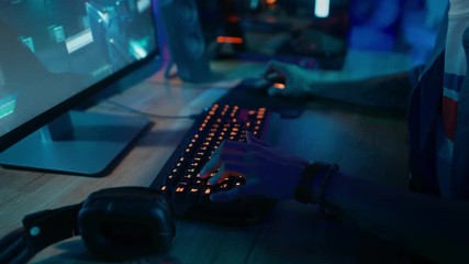 Wall Mural - Close Up Hands Shot Showing a Gamer Pushing the Keyboard Buttons while Playing an Online Shooter Video Game. Keyboard Led Lights Change Color in Rainbow Spectrum. Gamer is Wearing a Bracelet.