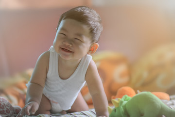 Cute asian baby boy under 1 year old has big smile on the bed in a cozy room with his toy and sunset light, processed in soft and selective focus