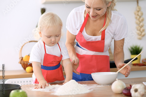 Plakat Mała dziewczynka i jej blondynki mama w czerwonych fartuchach bawić się i śmia się podczas gdy ugniatający ciasto w kuchni. Domowe ciasta na chleb, pizzę lub upiecz ciasteczka. Rodzinna zabawa i gotowanie koncepcji