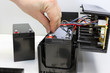 Male hand connects 12 volt battery in uninterruptible power supply. Repair and maintenance of UPS. Replacing battery.