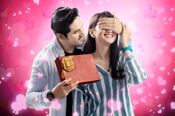 Wall Mural - Happy asian man covering his girlfriend eyes while giving her a gift