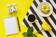 Wooden Cubes Calendar April 5th. Cup Of Coffee, Yellow Donut And Rose On Black And White Napkin, Empty Open Notepad For Text On Yellow Background. Concept Stylish Workplace