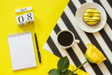 Wooden Cubes Calendar April 8th. Cup Of Coffee, Yellow Donut And Rose On Black And White Napkin, Empty Open Notepad For Text On Yellow Background. Concept Stylish Workplace