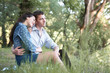 © soleg - young couple sitting on the grass in the forest and looking on sunset, summer nature, bright sunlight, shadows and green leaves, romantic feelings