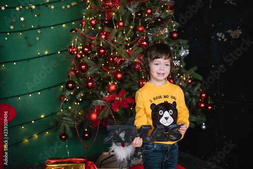 Fotografie, Obraz Little happy cute boy near the Christmas tree and holds a gift box