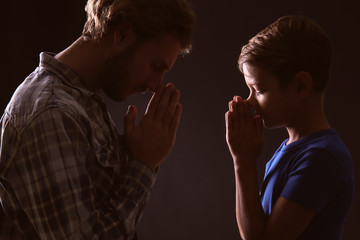 Wall Mural - Praying father and son on dark background