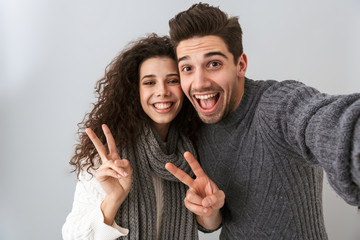 Portrait of happy man and woman taking selfie photo and gesturing with fingers, isolated over gray background