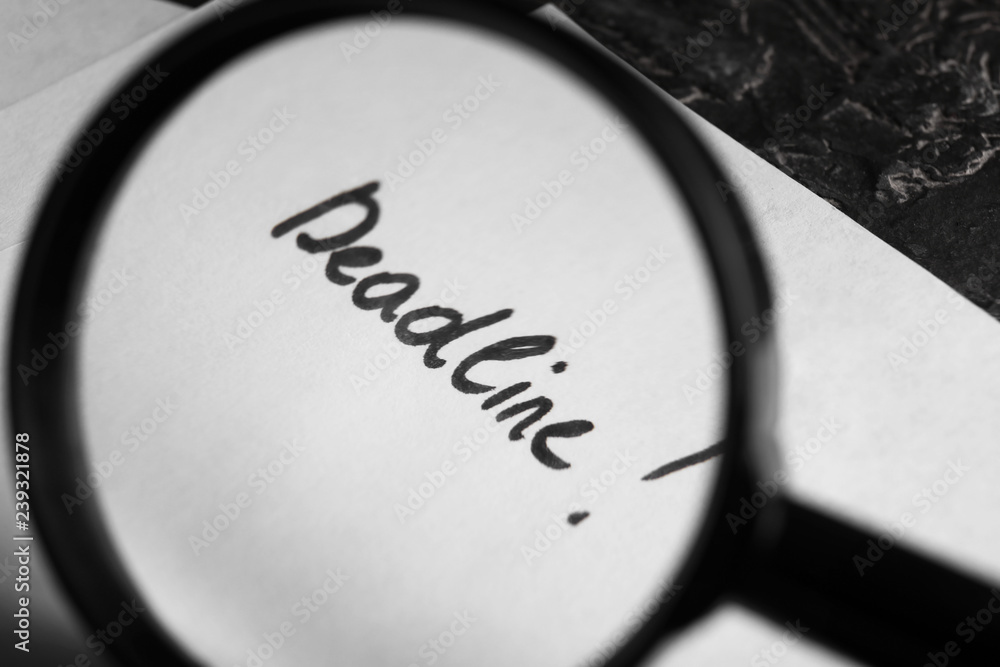 View on paper with word DEADLINE through magnifying glass, closeup