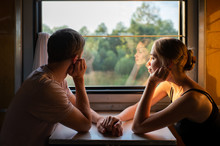 Couple Of Lovers Traveling In Train. Mood Portrait Of Romantic Pair In Wagon Looking At Window With Self Reflections In It. Adventure On Holiday Of Happy Friends. Man And Woman Looking At Each Other.