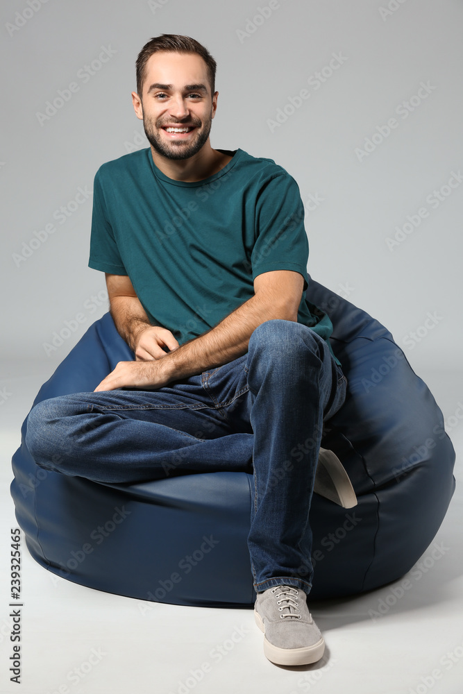 Young man sitting on beanbag chair against grey background
