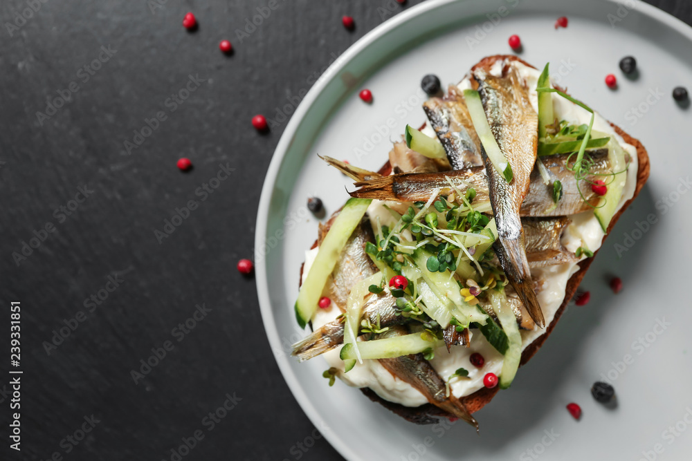 Tasty sandwich with sprats on dark table