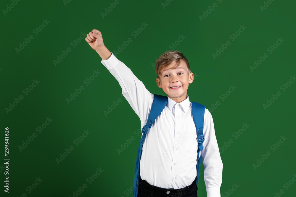 Happy little schoolboy with backpack on color background