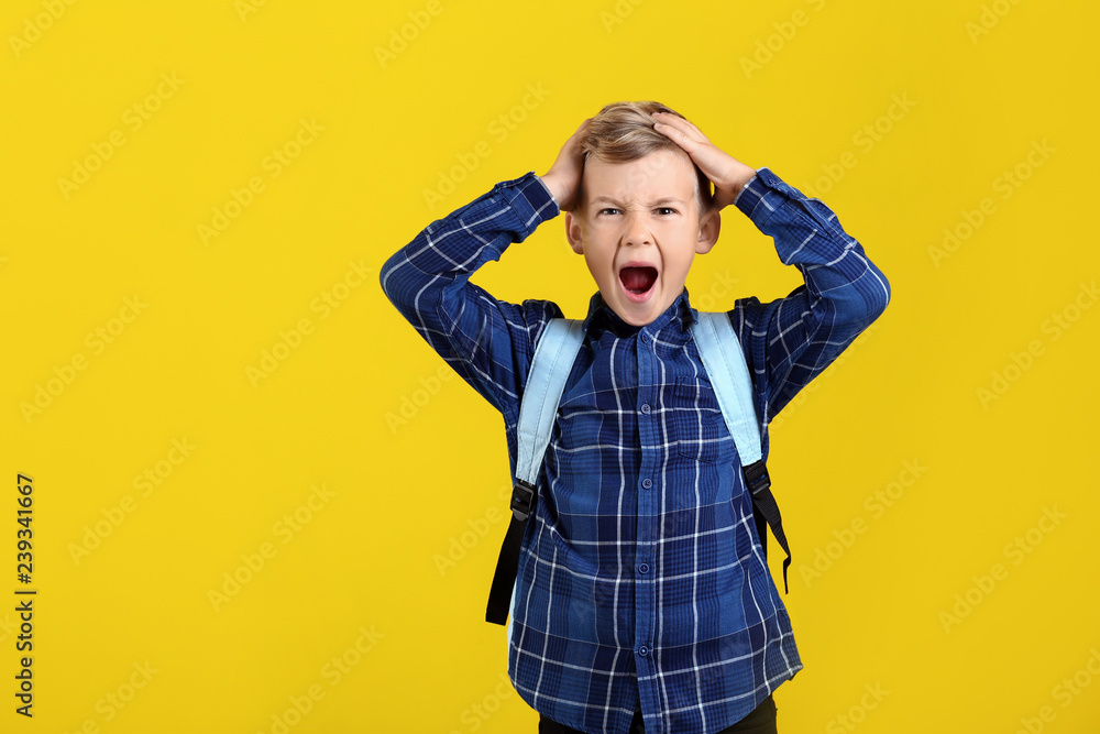Stressed little schoolboy with backpack on color background