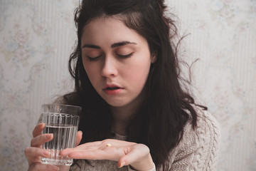 a young girl holds a glass of water in one hand and a small yellow pill in the other