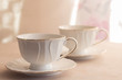 Tableware for tea party - two cups - on white tablecloth on light pink floral background with sunlight. Close-up, copy space