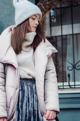 shopping, street fashion, style, people concept - model woman posing for photo outdoor. stylish hipster girl in warm Knitted winter cap and light jacket in the midst of street bustle on the streets