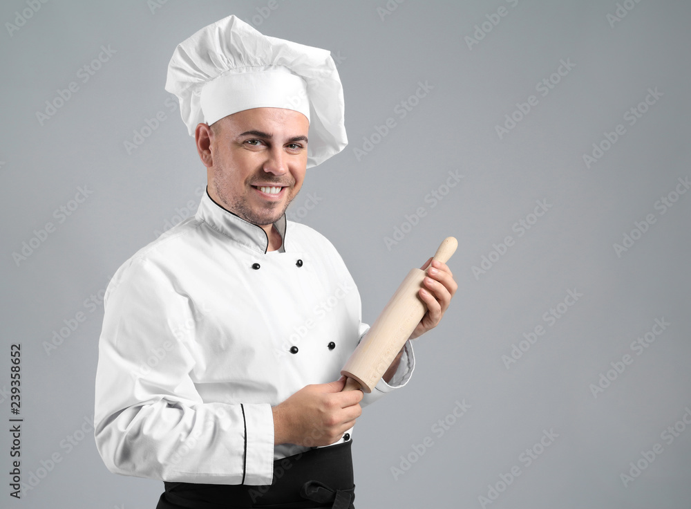 Male chef with rolling pin on grey background