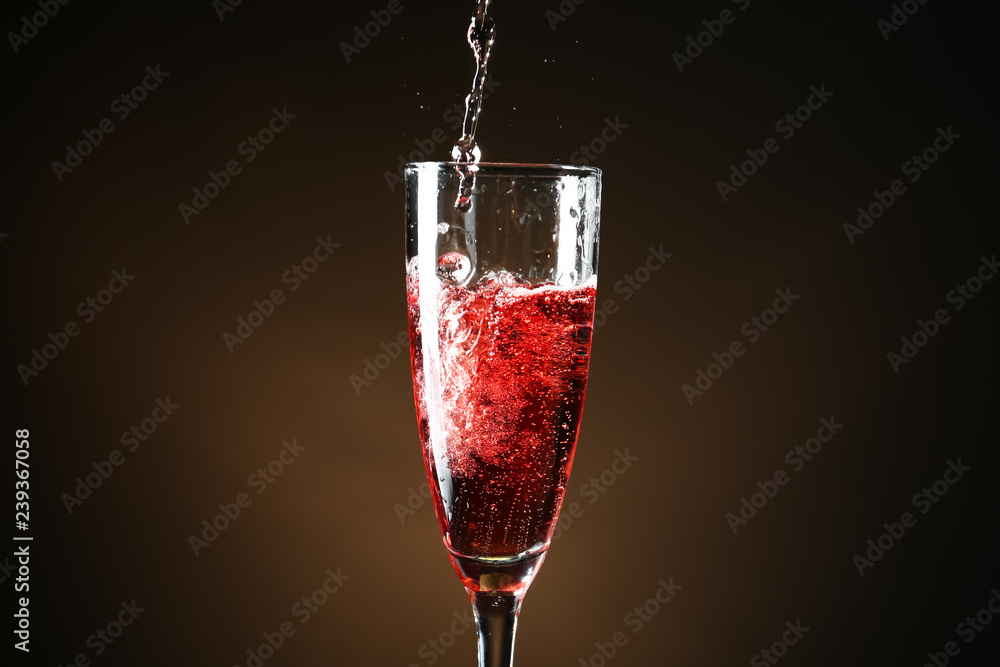 Pouring of champagne into glass on dark background