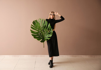 Beautiful woman with green tropical leaf near color wall