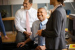 © Erickson Stock - Smiling mid-adult businessman smiling up at his colleague while seated at a desk in an office.