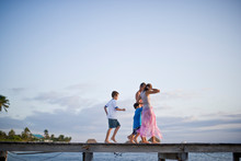 Couple And Their Sons Walking Along A Jetty Over Water.