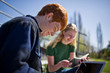 © Erickson Stock - Smiling teenage boy on his laptop while sitting outside with his girlfriend.