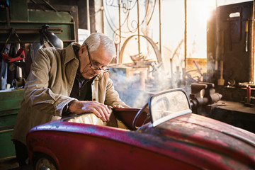 Senior man in his workshop repairing an old fashioned pedal car 