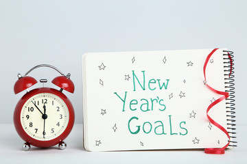 New year goals in notepad with alarm clock on grey background