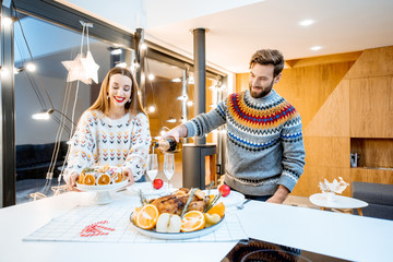 Young couple having festive dinner sitting together in the modern house during the winter holidays