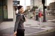 © Erickson Stock - Smiling mid-adult businesswoman looking over her shoulder and carrying a folder of documents while crossing a street in the city.