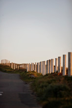 Wooden Fence Posts Along A Road Near A Beach At Sunset.