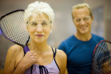 Portrait Of A Senior Woman Holding A Squash Racket While Standing With Her Playing Partner.