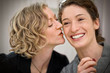 © Erickson Stock - Smiling young woman being kissed by her girlfriend on the cheek.