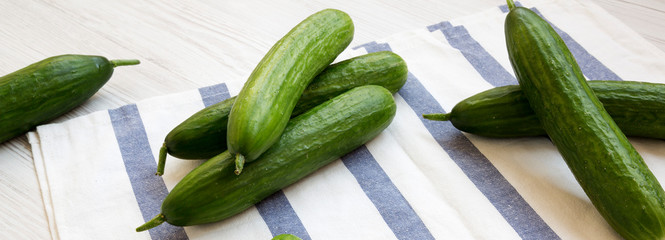 Fresh raw organic green cucumbers on white wooden background, side view. Closeup.