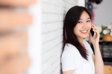 Beautiful of portrait young asian woman talk smart phone and smile standing on cement brick background, freelance female calling telephone, communication of mobile concept.