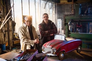 A senior man and his son at workshop to restore an old pedal car