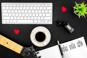 Guitar with paper note, keyboard and coffee in music studio for dj or musician work black background top view