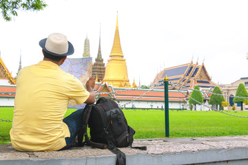 Traveler man and woman with a backpack in temple. They are siting and see The Grand Temple Palace in Bangkok. Man is pointing it.Thailand.holiday, vacation , Photo Travel and relax time concept.