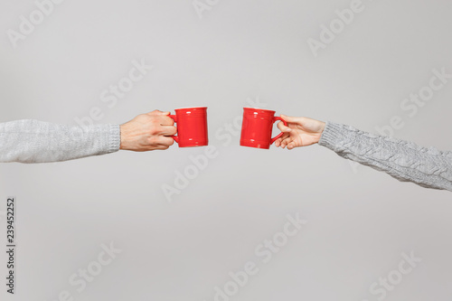 Fotomural Close up cropped of woman, man two hands horizontal holding red cups of tea, clinking isolated on grey wall background
