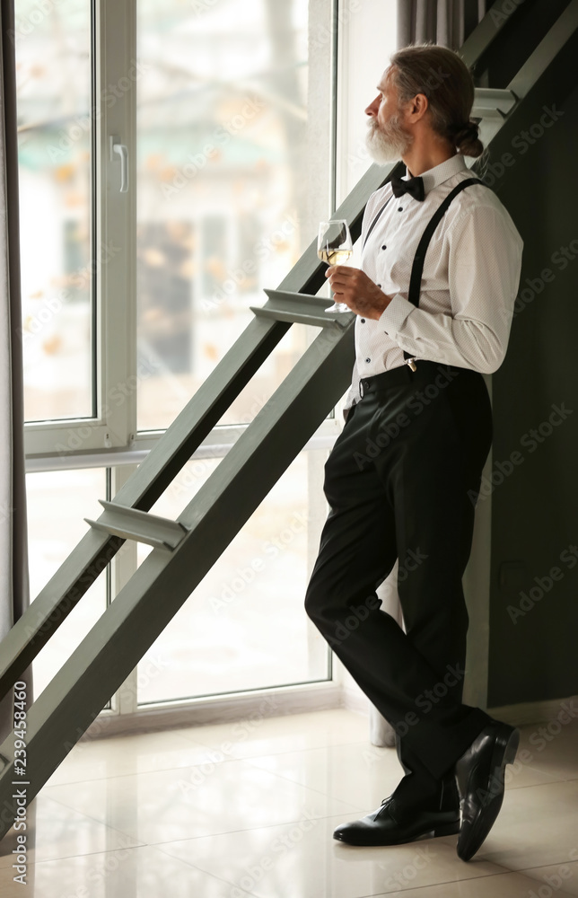 Senior gentleman drinking wine near window at home