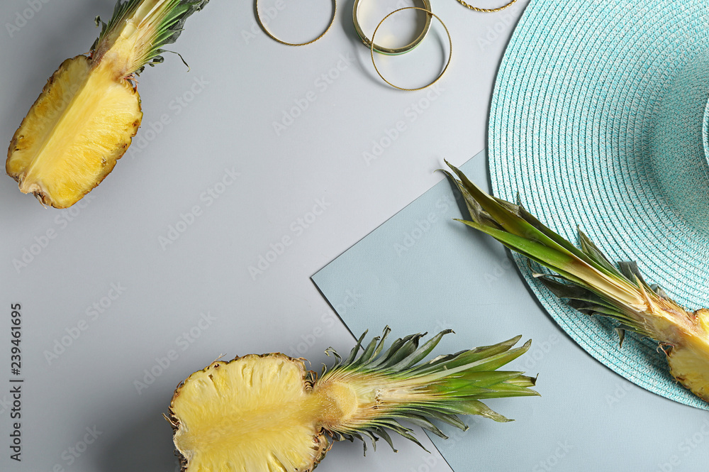 Ripe tasty pineapples and beach hat on grey background