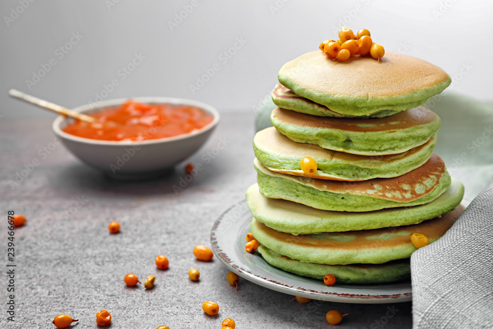 Tasty green pancakes with sea-buckthorn on grey table
