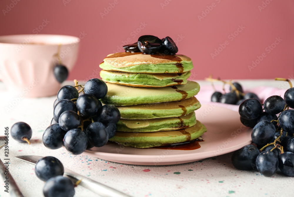 Tasty green pancakes with grapes on table