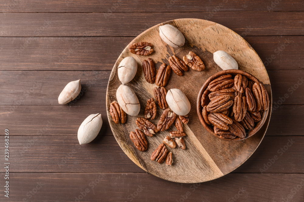 Plate with pecan nuts on wooden background