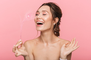 Happy cheerful young woman posing isolated over pink wall background holding feather leaf.