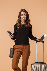 Canvas Print - Image of caucasian woman 20s with baggage holding mobile phone and travel ticket, isolated over beige background